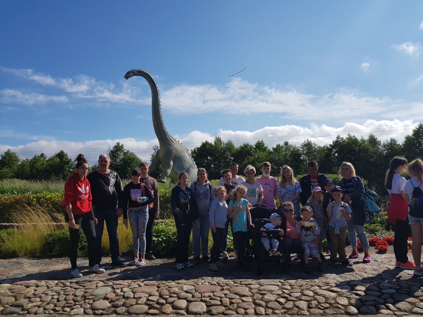 zdjęcie grupowe uczestników wycieczki na tle makiety dużego dinozaura