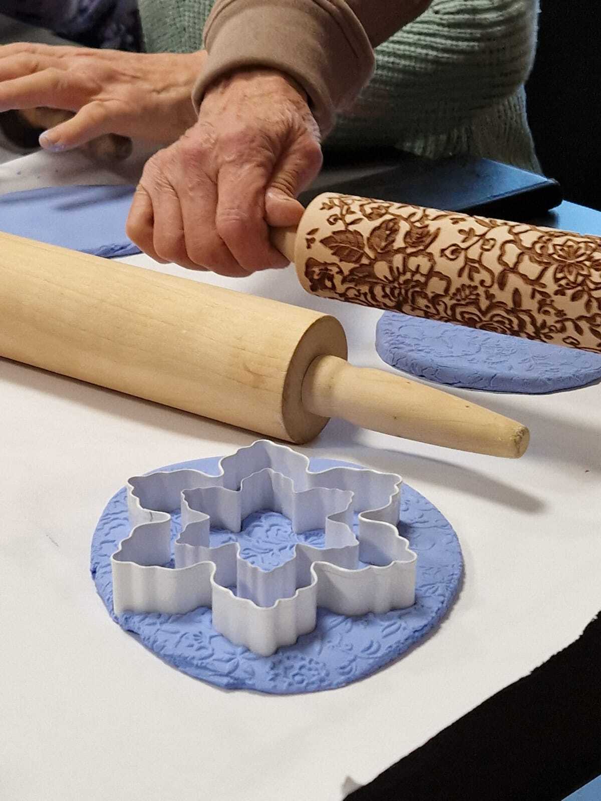 uczestniczka warsztatów z wałkiem w dłoniach przy wspólnym stole tworzące ozdoby ceramiczne