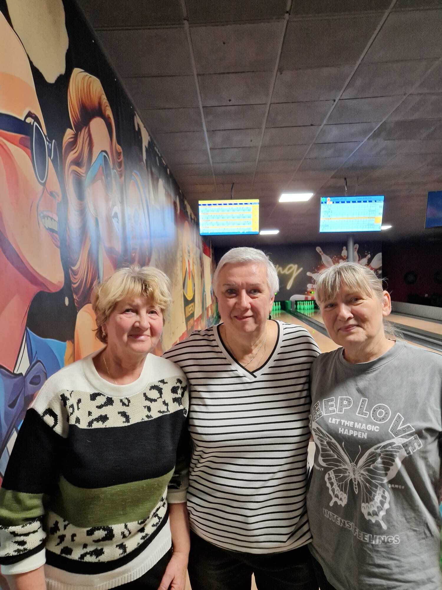 zdjęcie przedstawia trzy uczestniczki spotkania stojące obok siebie, w tle tory do gry w kręgle