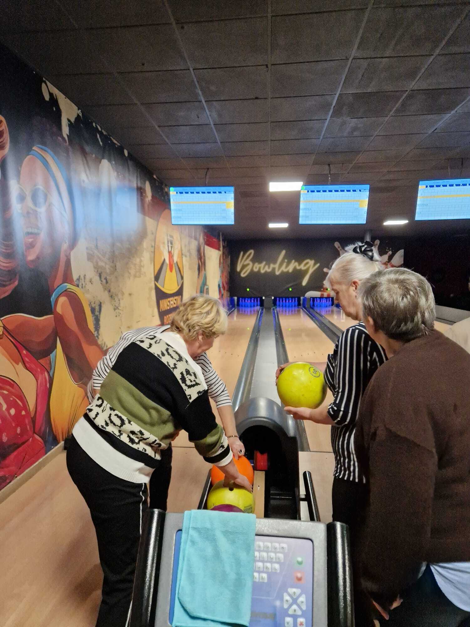 zdjęcie przedstawia cztery uczestniczki spotkania wybierające kule do gry w kręgle, w tle tory do gry w kręgle