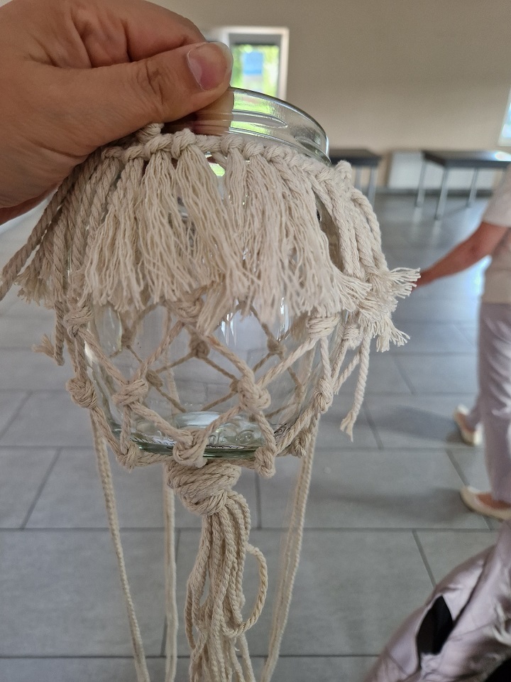 zdjęcie przedstawia mały lampion - szklany słoik w koszyczku ze sznurka