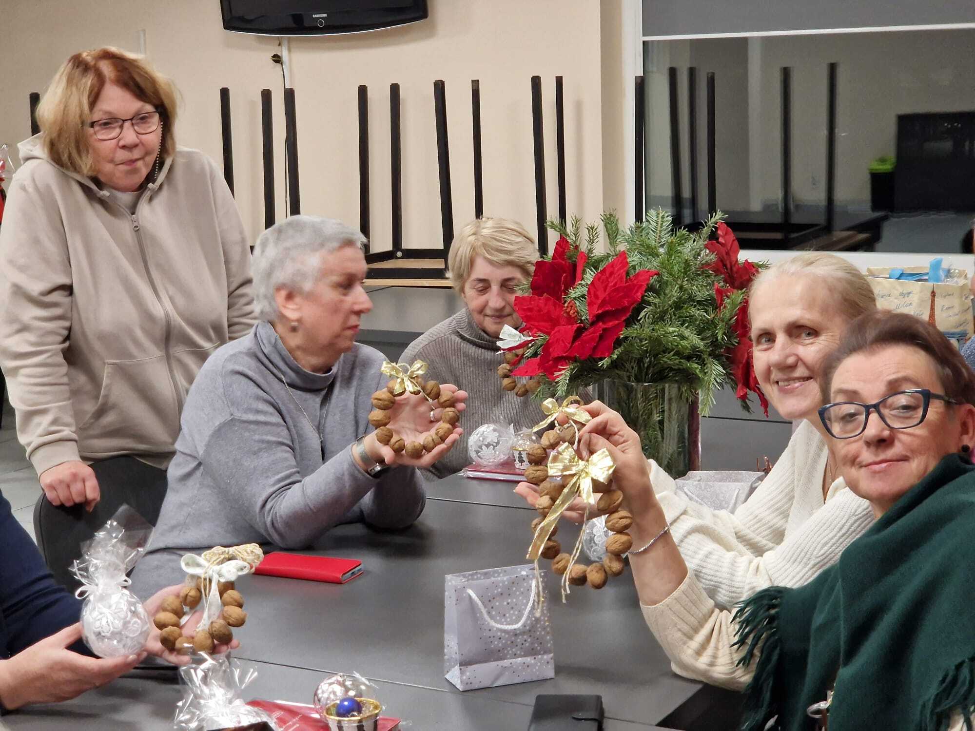 cztery uczestniczki warsztatów siedżace przy stole prezentujące w dłoniach gotowe ozdoby z orzechów włoskich