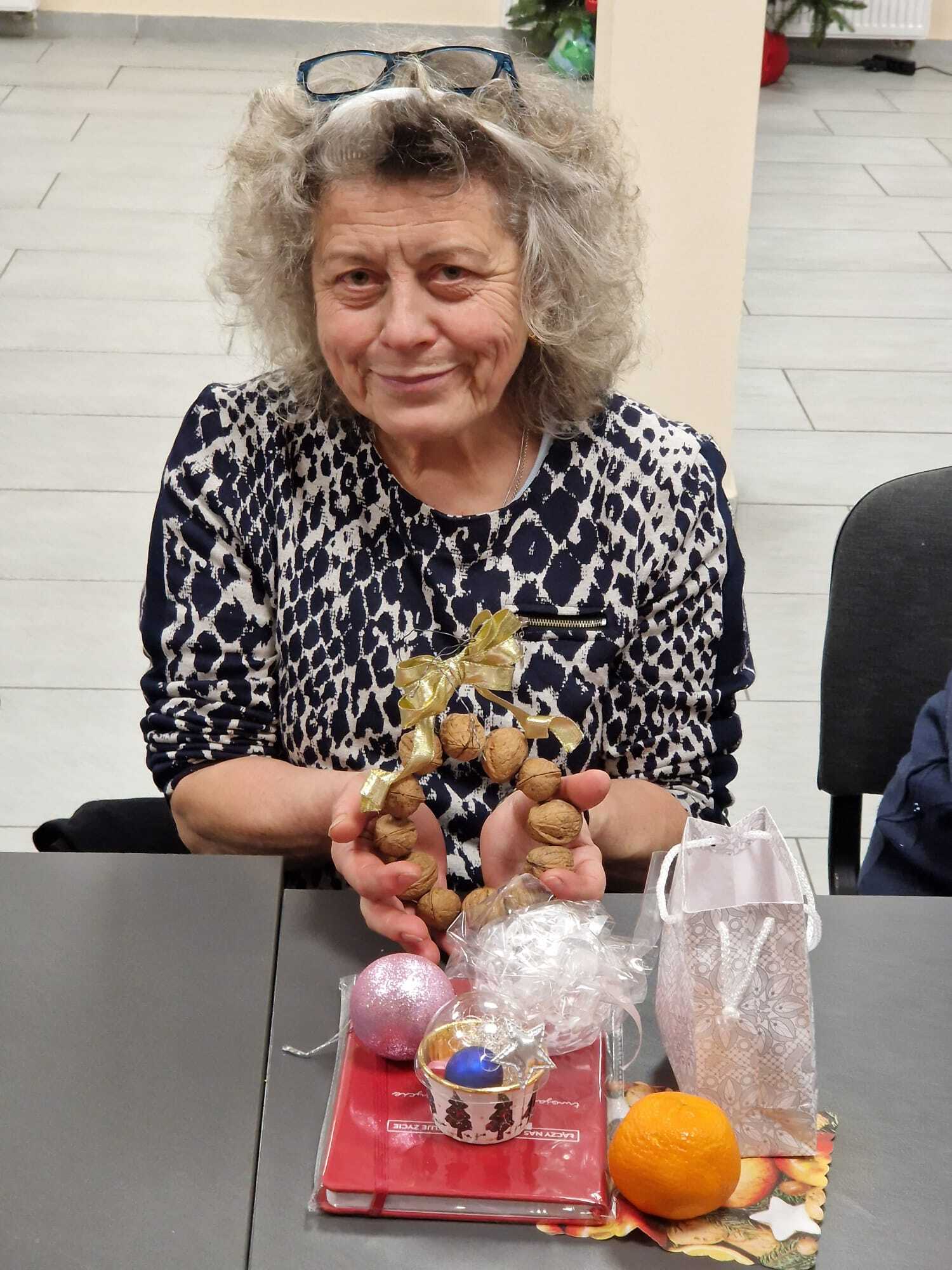 uczestniczka warsztatów siedząca przy stole prezentująca w dłoniach gotową ozdobę z orzechów