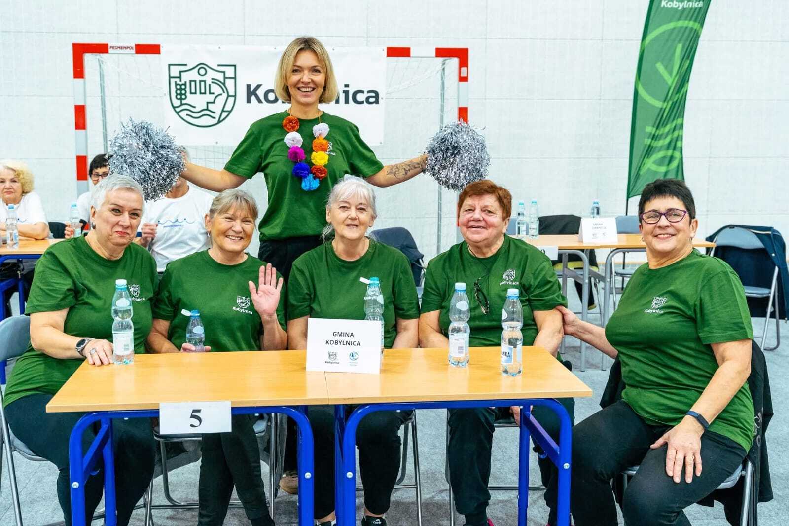 zdjęcie przedstawia drużynę Kobylnicy siedzącą przy stole wraz z stojącą panią Burmistrz Anną Gliniecką - Woś