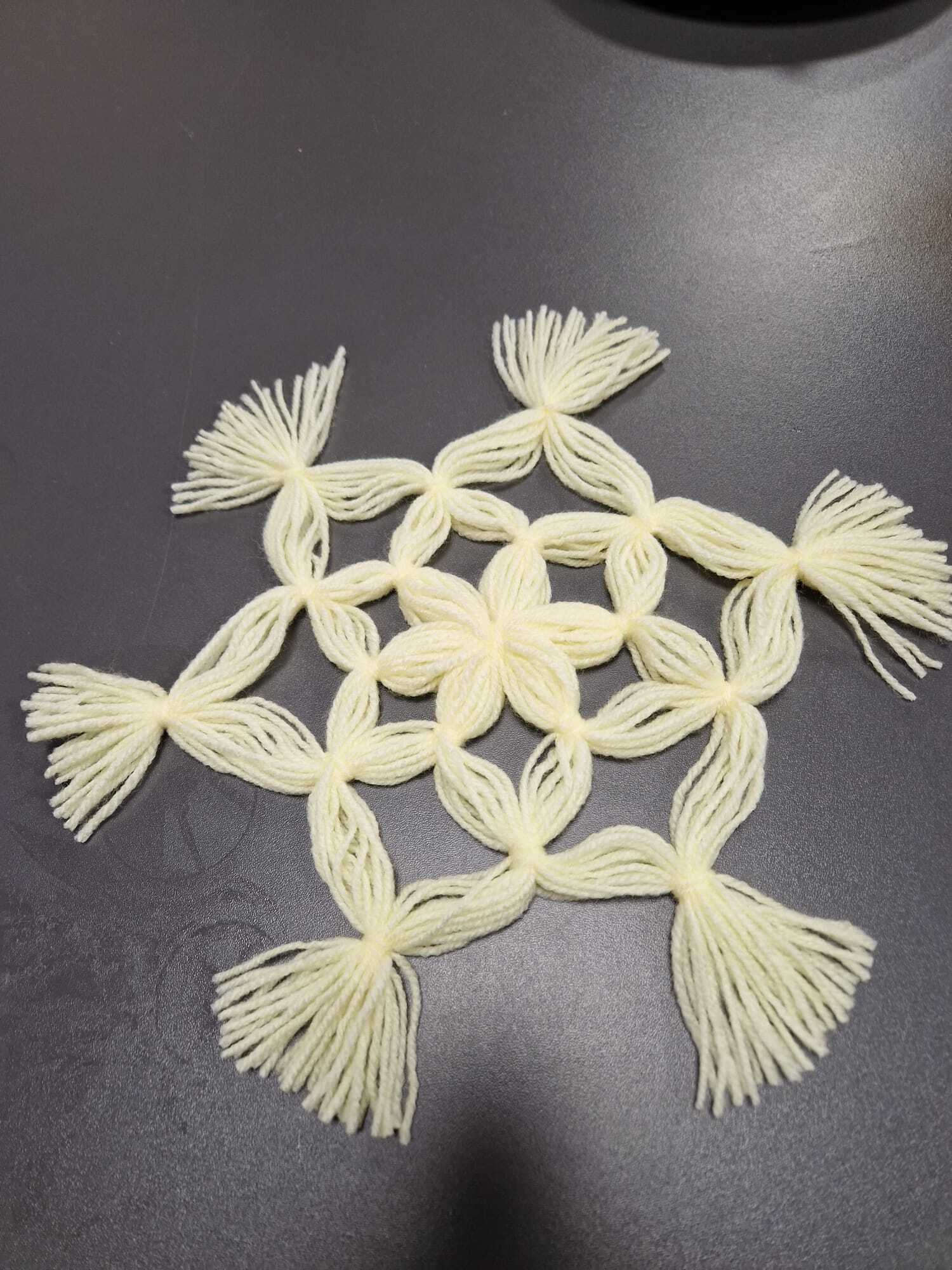 leżąca na blacie stołu gotowa ozdoba z włóczki w formie śnieżynki