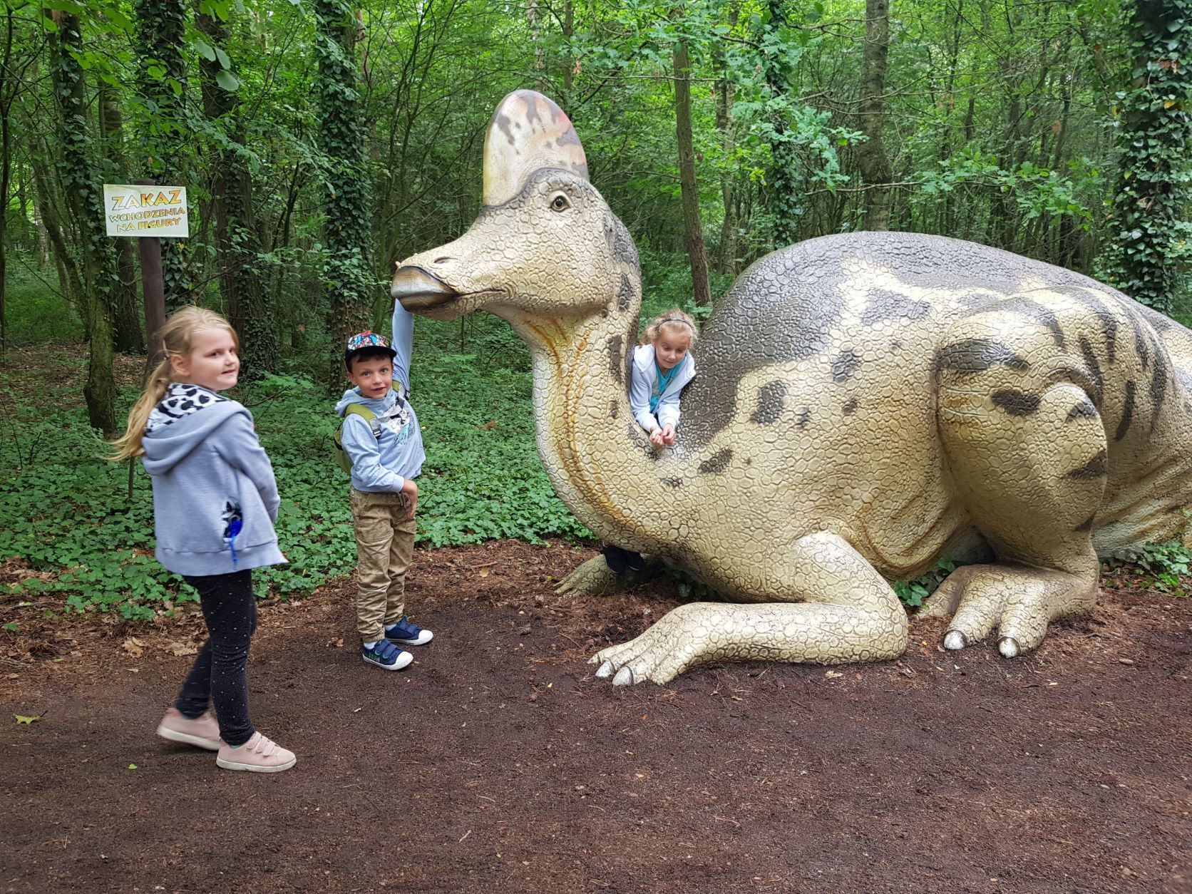 trójka dzieci przy makiecie dinozaura