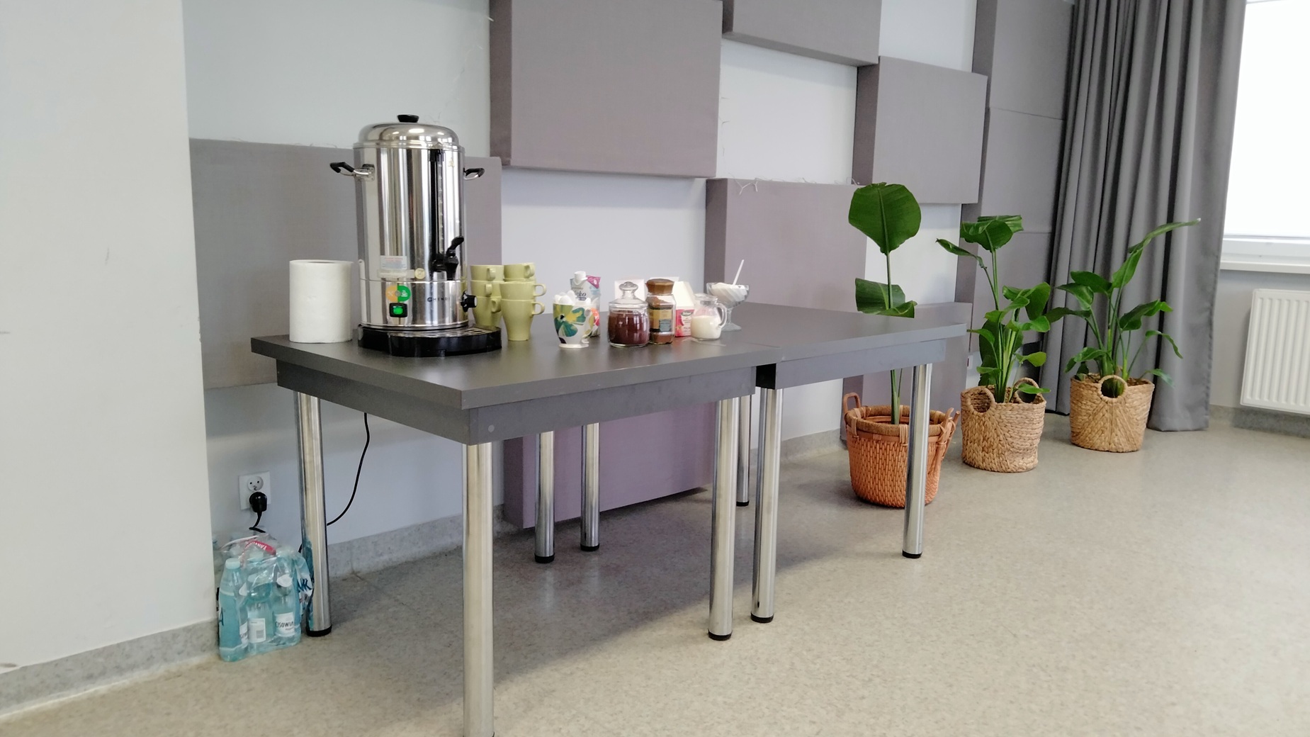 stolik, na którym znajduje się podgrzewacz wody, kubki, kawa, herbata, śmietanka do kawy, poczęstunek dla uczestnikow spotkania