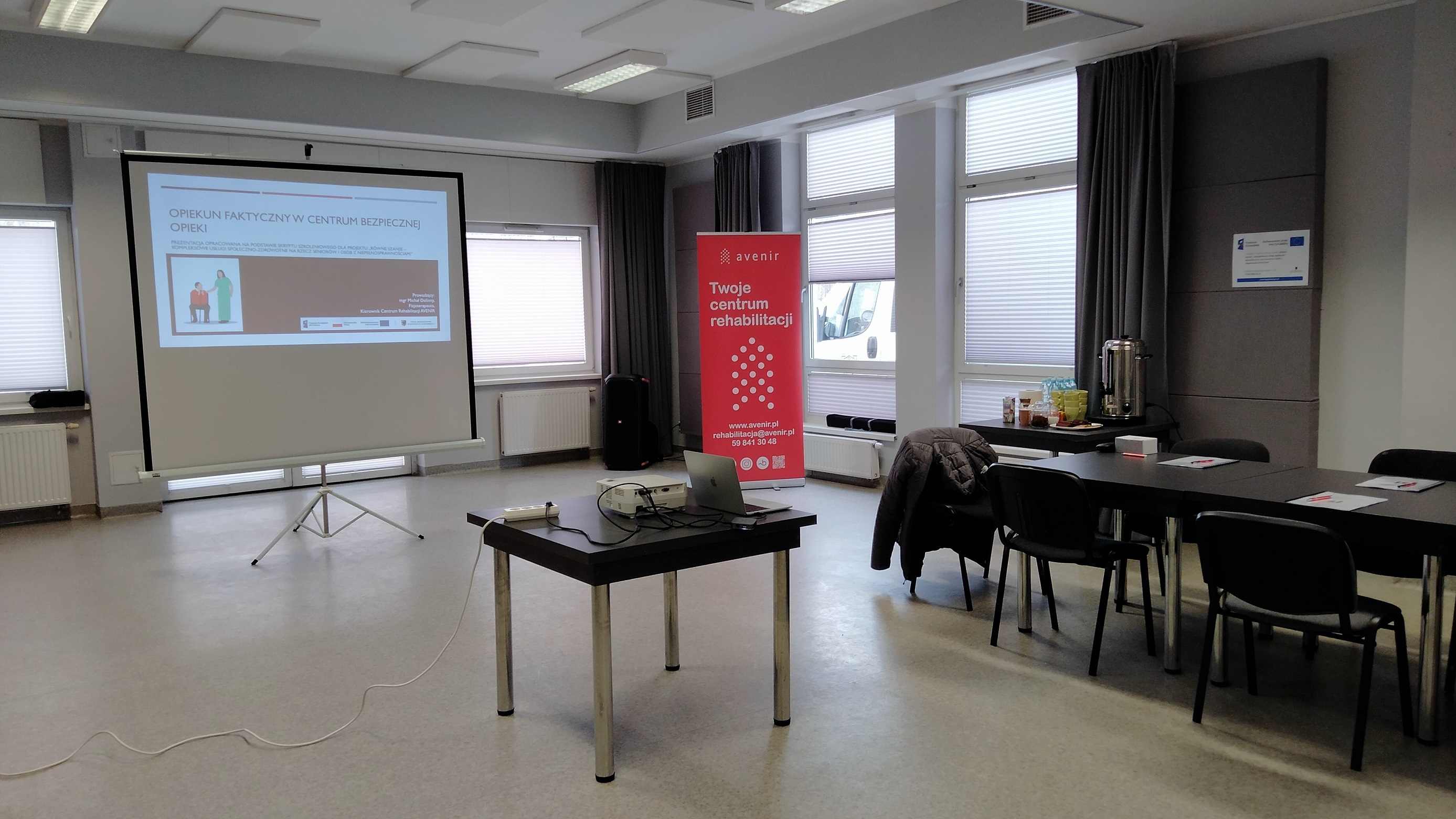 fotografia przedstawia przygotowaną do szkolenia salę z projektorem i wolnostojącym ekranem projekcyjnym, stolikiem kawowym i miejscami siedzącymi dla uczestników spotkania